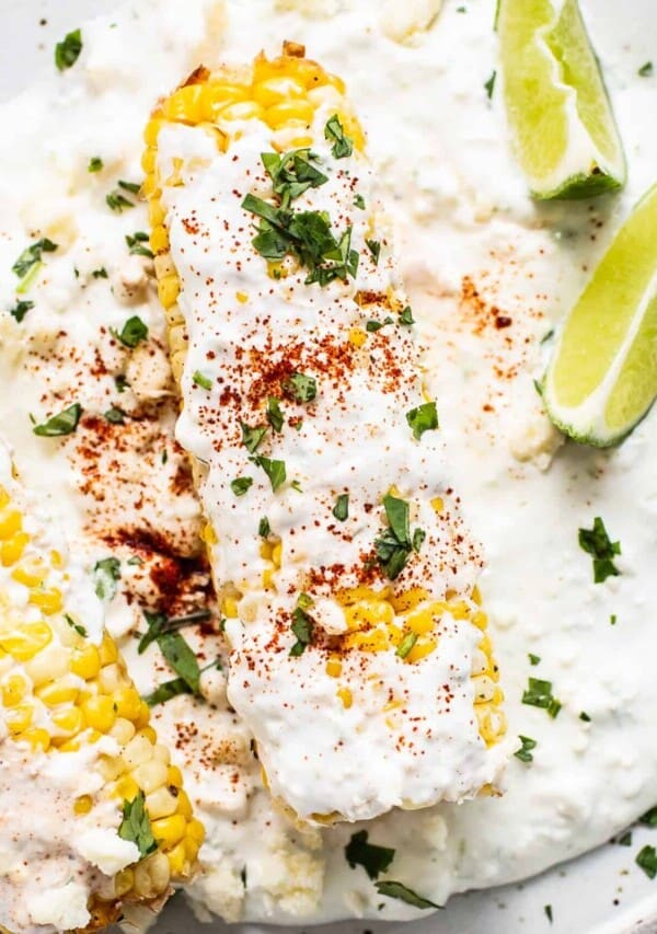 Air fryer elote on a plate with slices of lime.