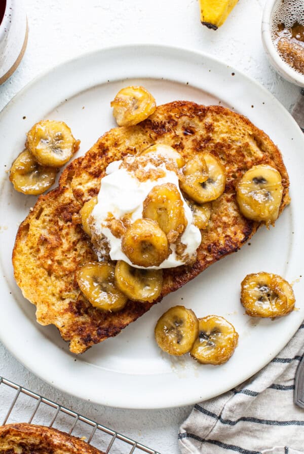 A plate of french toast with bananas and whipped cream.