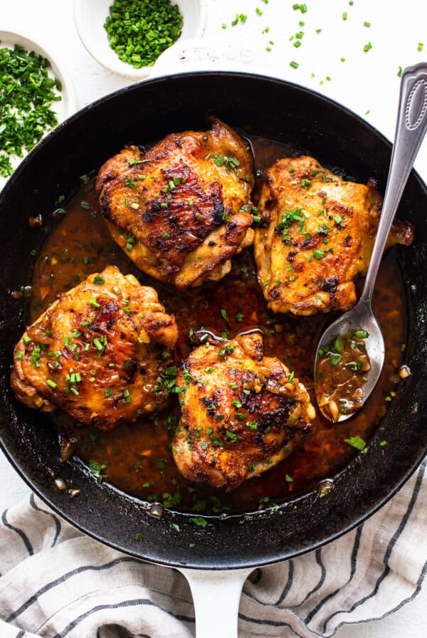 Chicken thighs in a skillet with sauce and herbs.