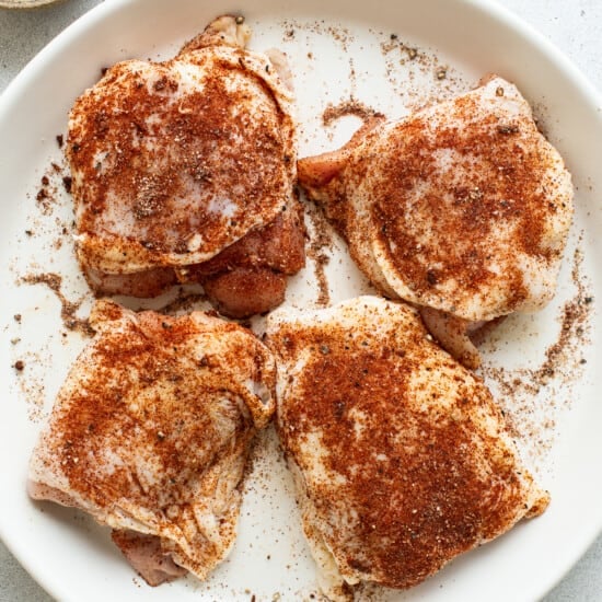 Four chicken breasts on a white plate with spices.