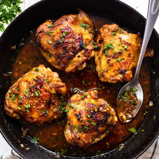 Chicken thighs in a skillet with sauce and herbs.