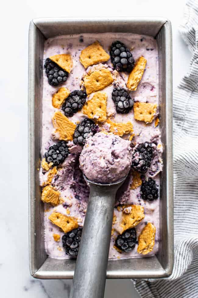 Baking pan full of blackberry cheesecake cottage cheese ice cream with cookie and blackberry sprinkled on top.