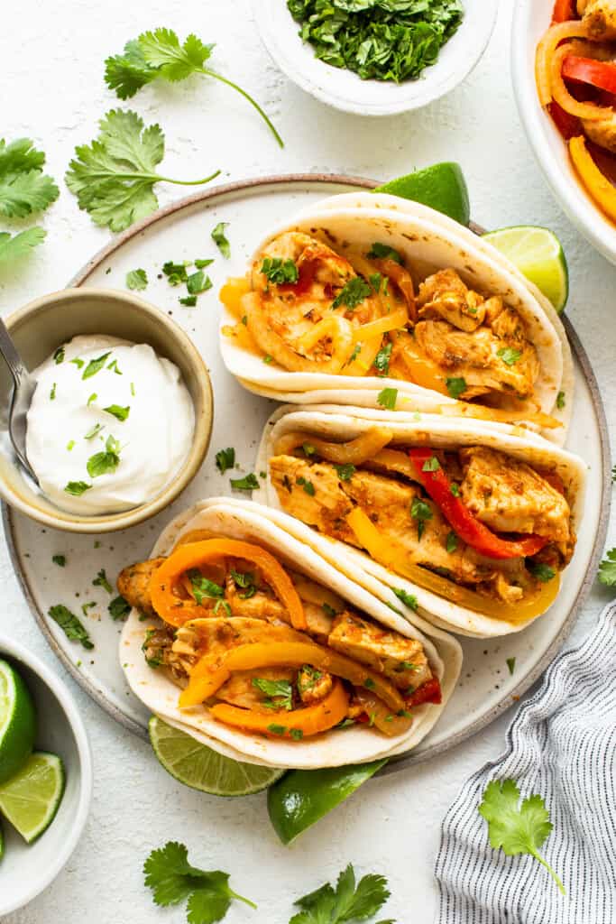 Chicken fajita tacos on a plate with limes and sour cream.
