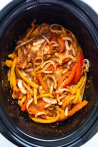 A slow cooker filled with peppers and onions.