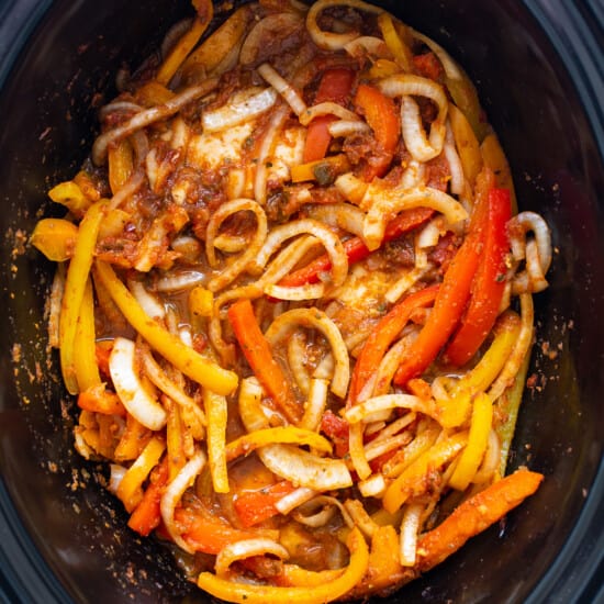 A slow cooker filled with peppers and onions.
