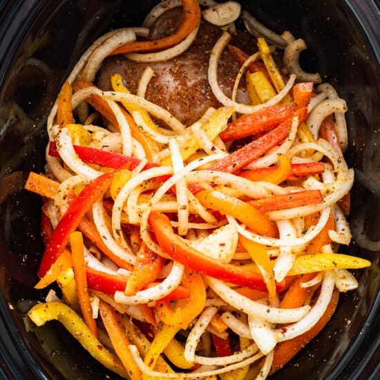 A crock pot filled with peppers and onions.