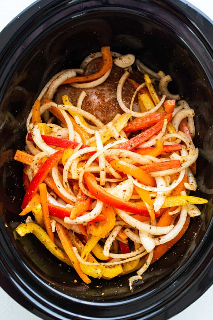 A crock pot filled with peppers and onions.