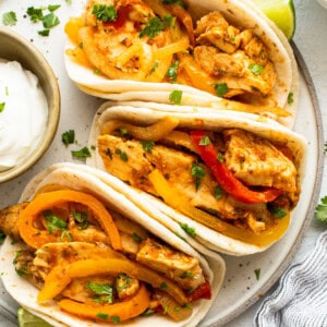 Three chicken tacos with peppers and sour cream on a plate.