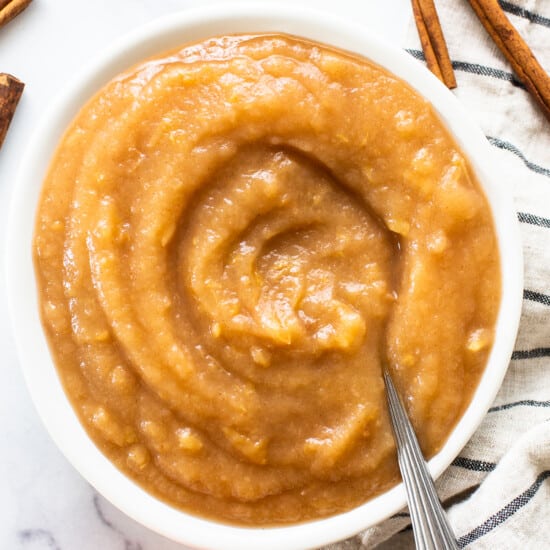 Apple butter in a white bowl with cinnamon sticks.