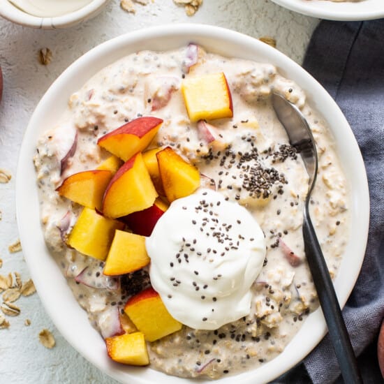 A bowl of oatmeal with peaches and yoghurt.