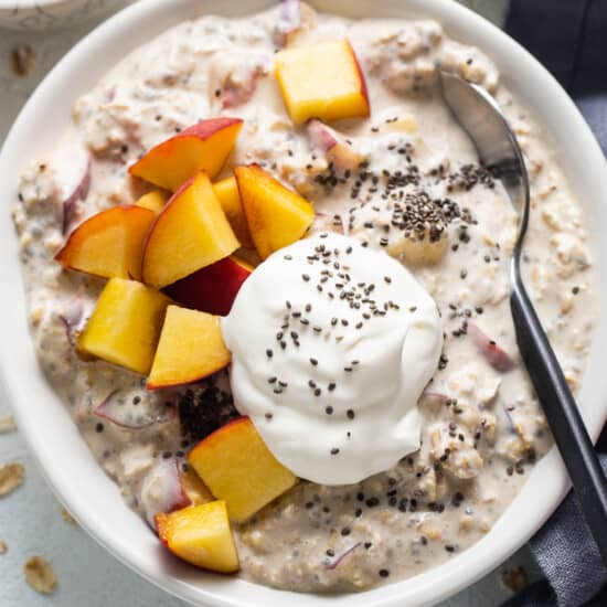 A bowl of oatmeal with peaches and whipped cream.
