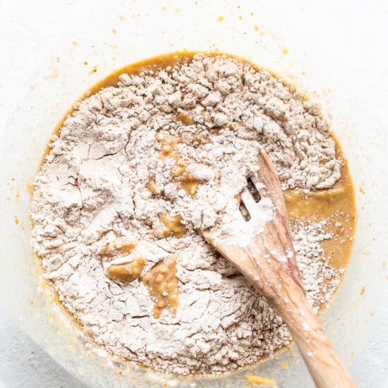 A bowl of flour with a wooden spoon in it.