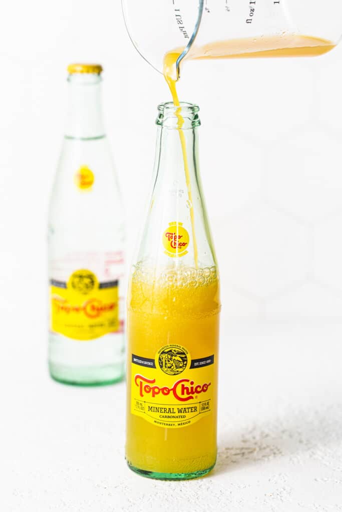 Mango juice being poured into a topo chico bottle.