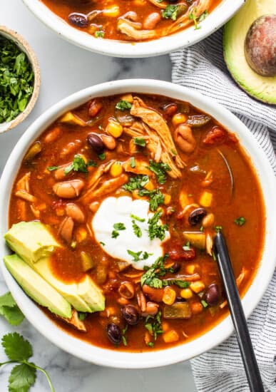Two bowls of chicken enchilada soup garnished with avocado and sour cream.