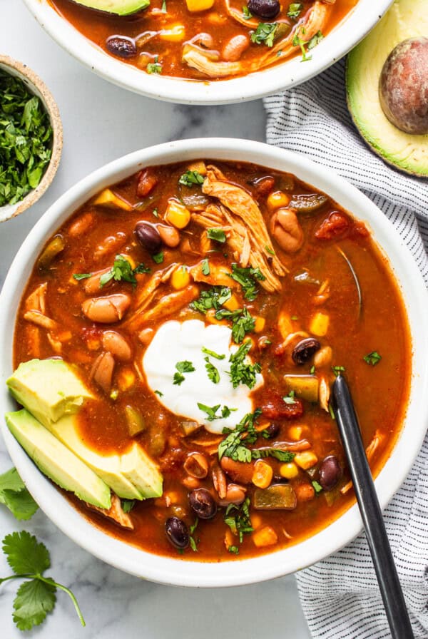 Two bowls of chicken enchilada soup garnished with avocado and sour cream.