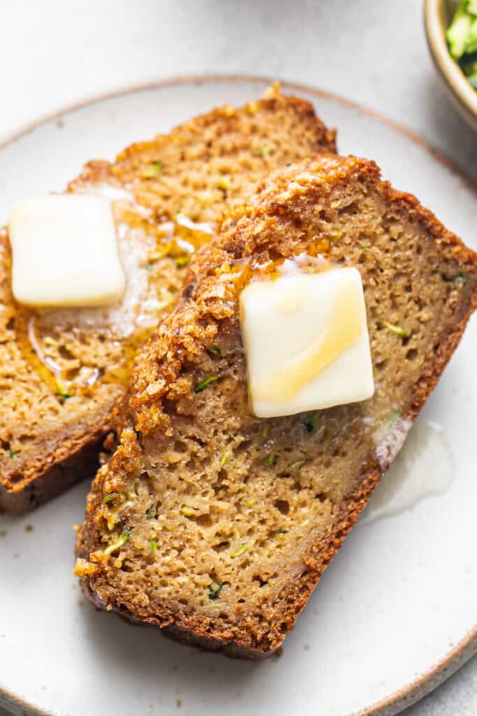 two slices of zucchini bread with butter on a plate.
