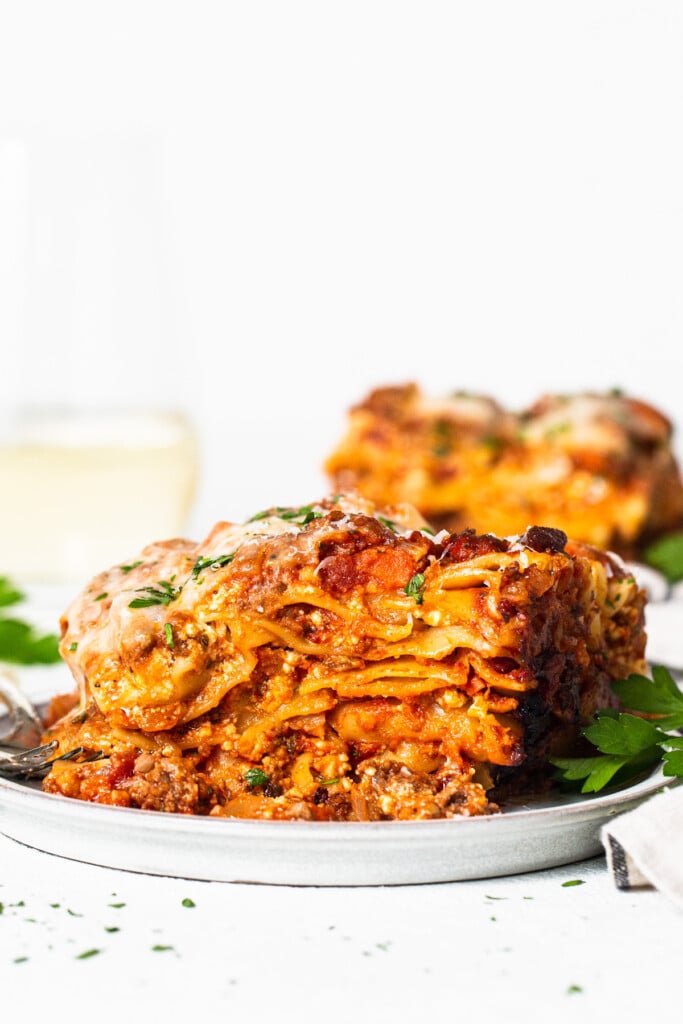 a white plate topped with lasagna next to a gl، of wine.