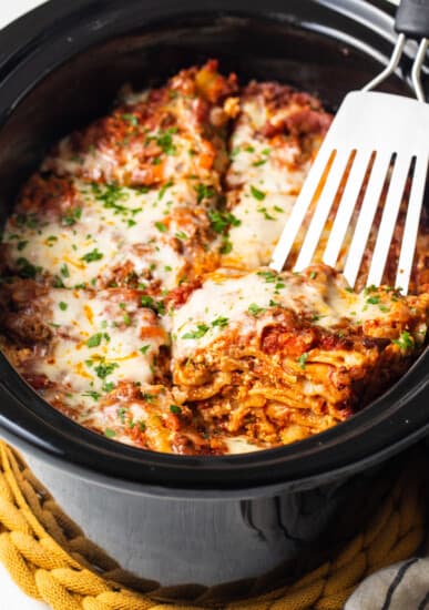 a close up of a fork in a crock pot filled with lasagna.