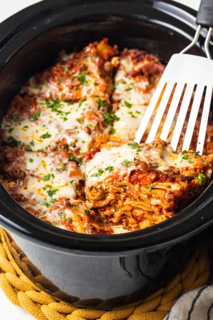 a close up of a fork in a crock ، filled with lasagna.