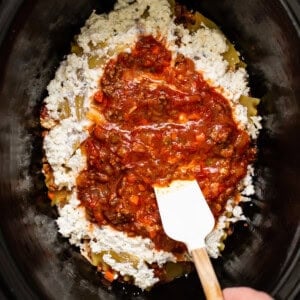 a person stirring a mixture of food in a crock pot.