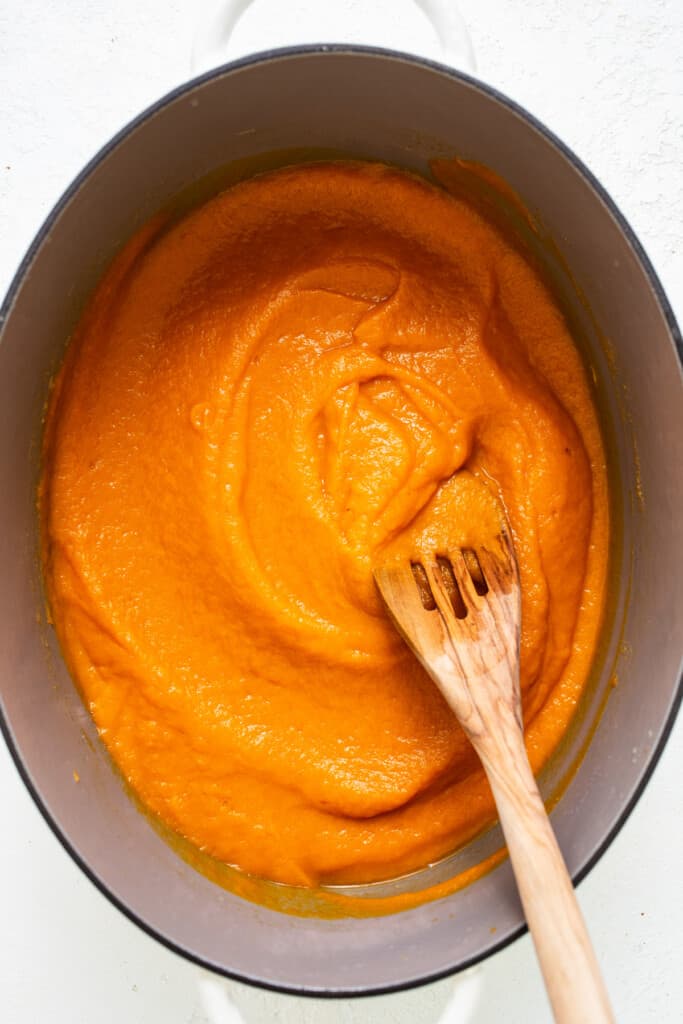a wooden spoon in a pot of orange sauce.