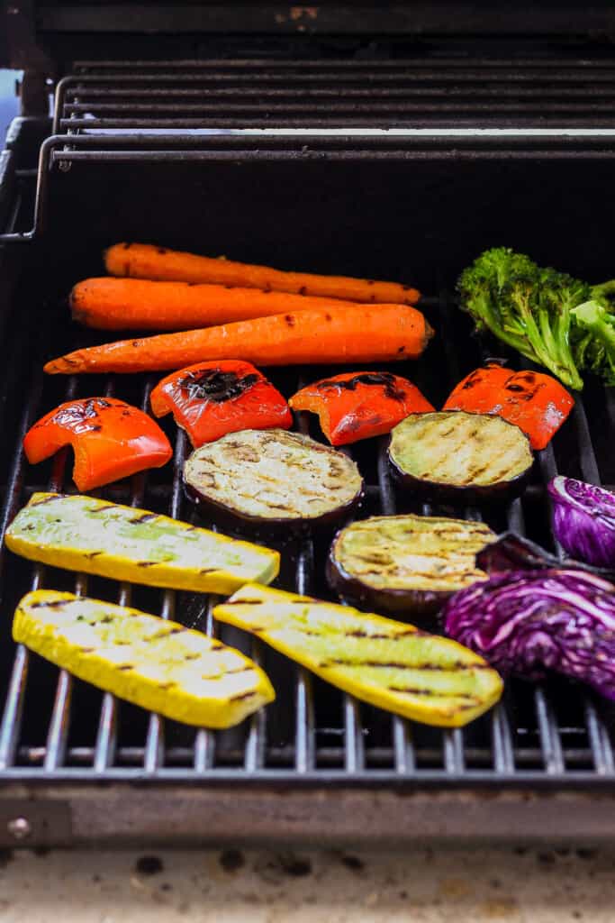 a bbq with carrots, broccoli, and other vegetables cooking on.