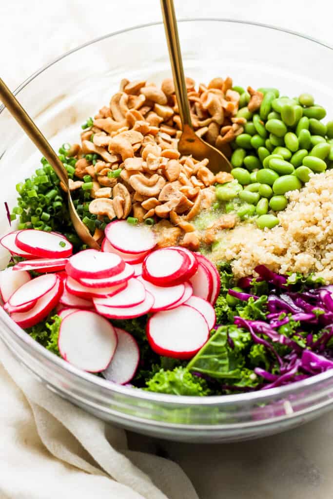 a bowl filled with greens, radishes, and cashews.