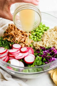 a person pouring dressing into a bowl of greens and radishes.