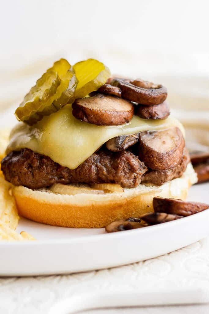 a burger with mushrooms and pickles on a plate.