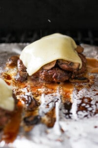 two burgers with cheese and mushrooms on top of foil.