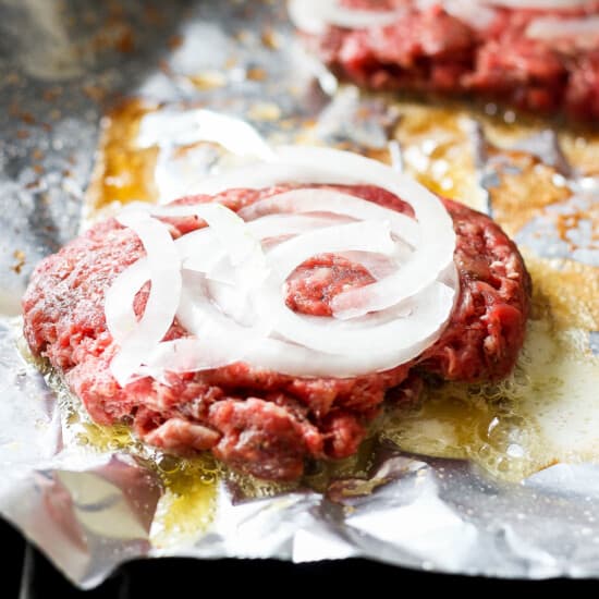 beef burgers with onions on foil.