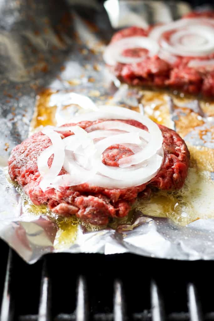beef burgers with onions on foil.