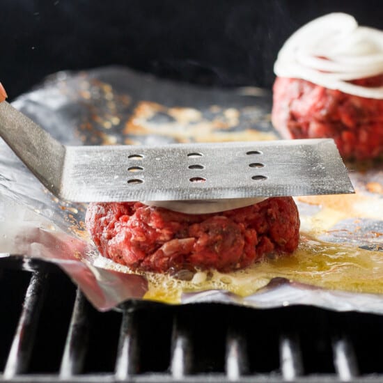 a person is slicing burgers on a grill.