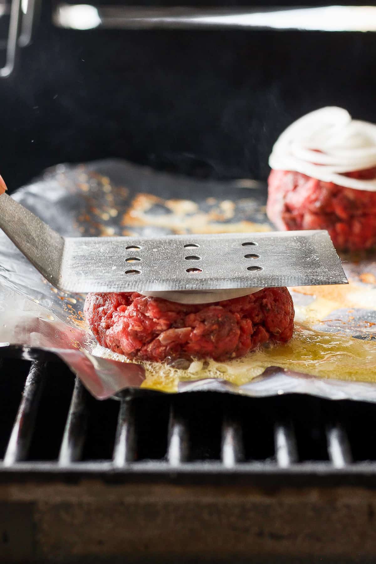 a person is slicing burgers on a grill.