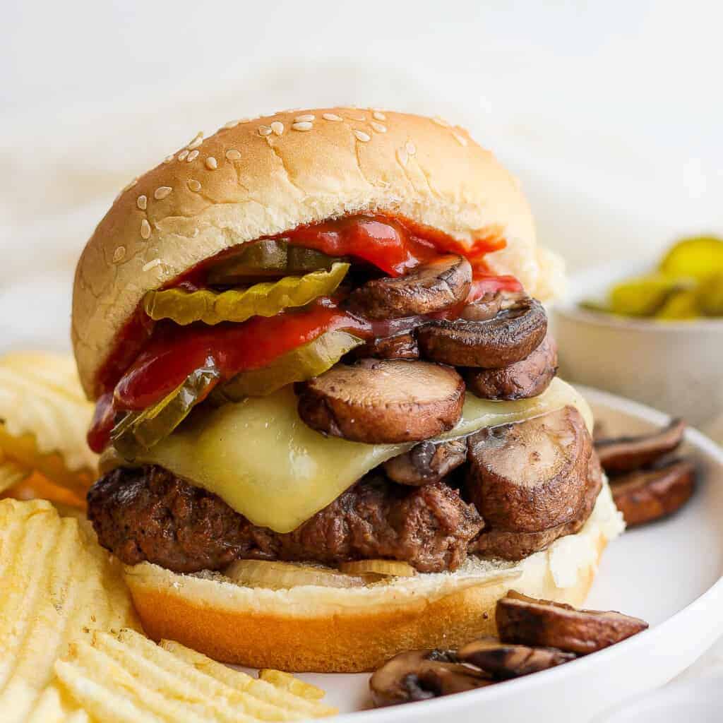 a burger with mushrooms, cheese and pickles on a plate.