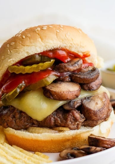 a burger with mushrooms, cheese and pickles on a plate.