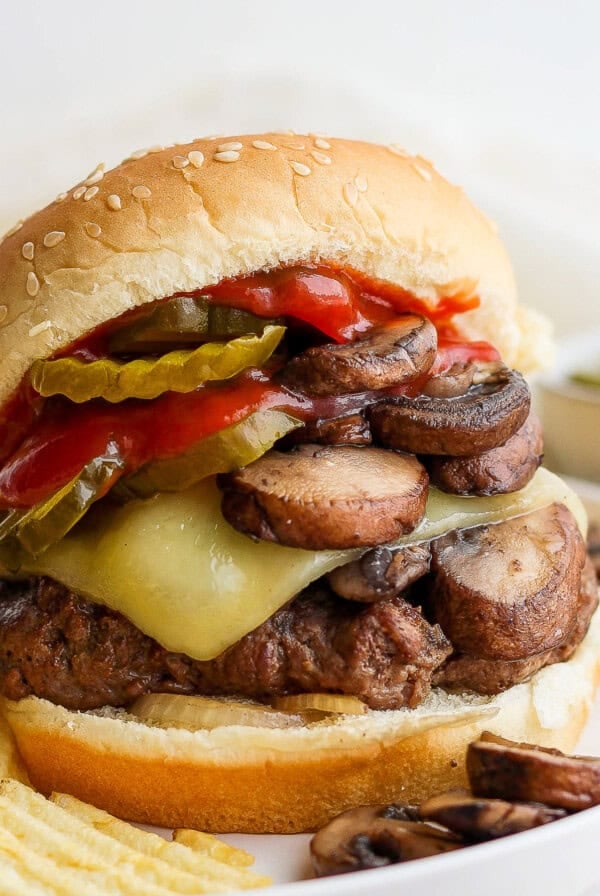a burger with mushrooms, cheese and pickles on a plate.