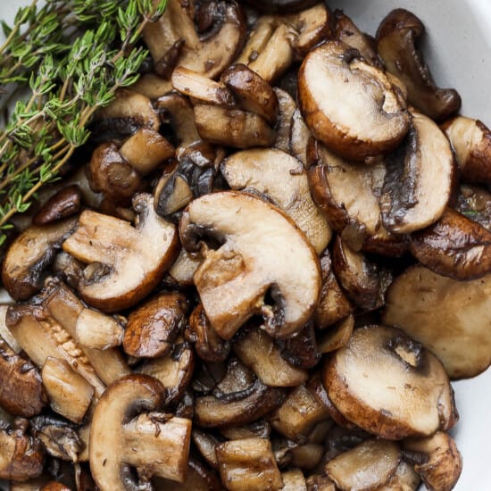 roasted mushrooms in a white bowl with a sprig of thyme.
