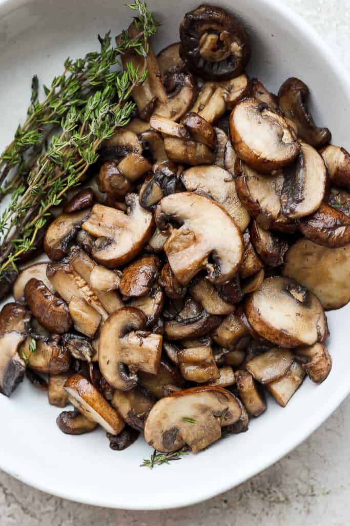 mushrooms in a white bowl with a sprig of thyme.
