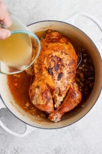 a person pouring liquid over a chicken in a pot.