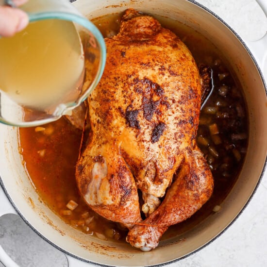 a person pouring liquid over a chicken in a pot.