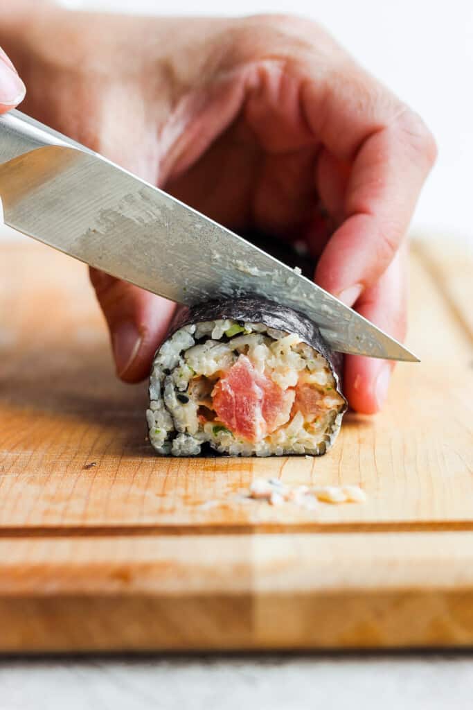 a person cutting sushi with a knife on a cutting board.