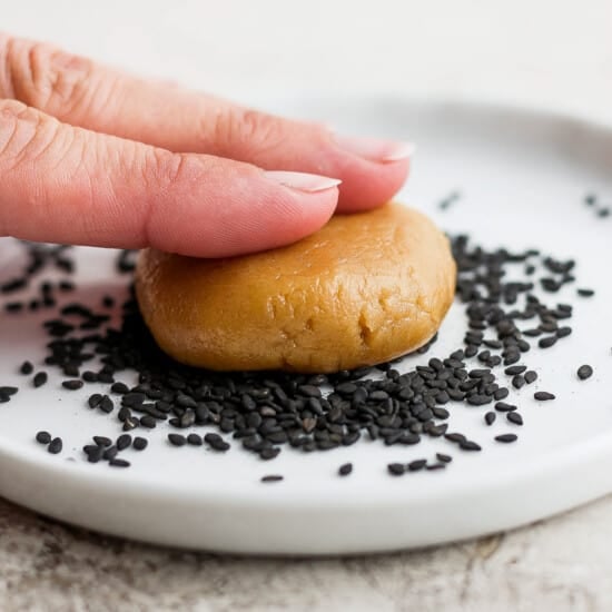 a hand is holding a cookie with sesame seeds on it.