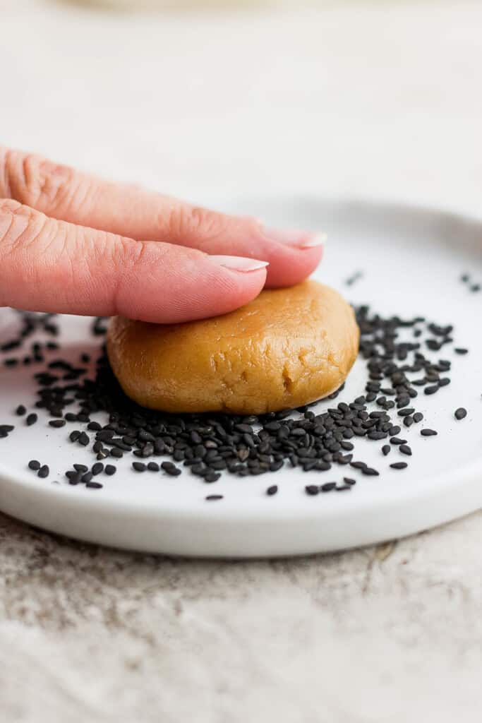 a hand is holding a cookie with sesame seeds on it.