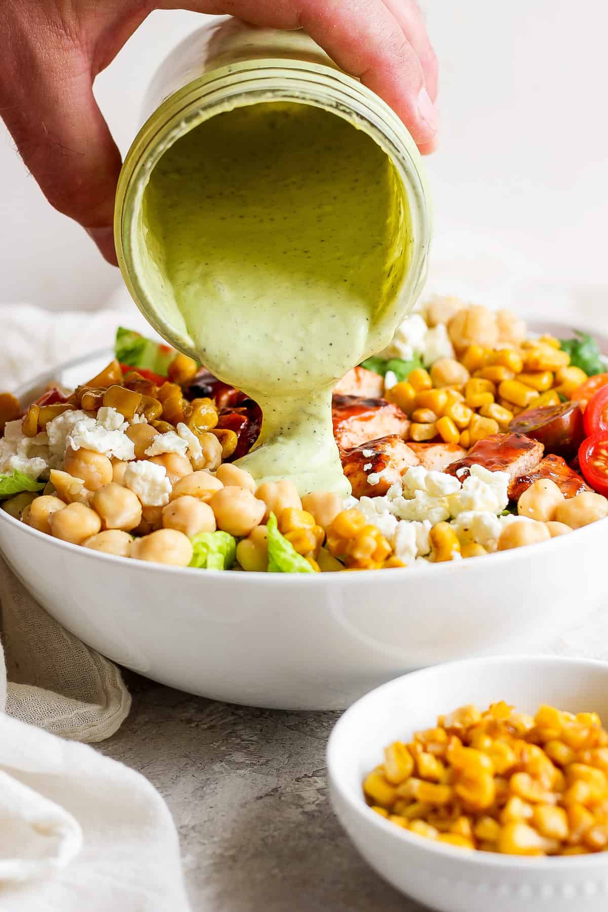 a person pouring a dressing into a bowl of salad.