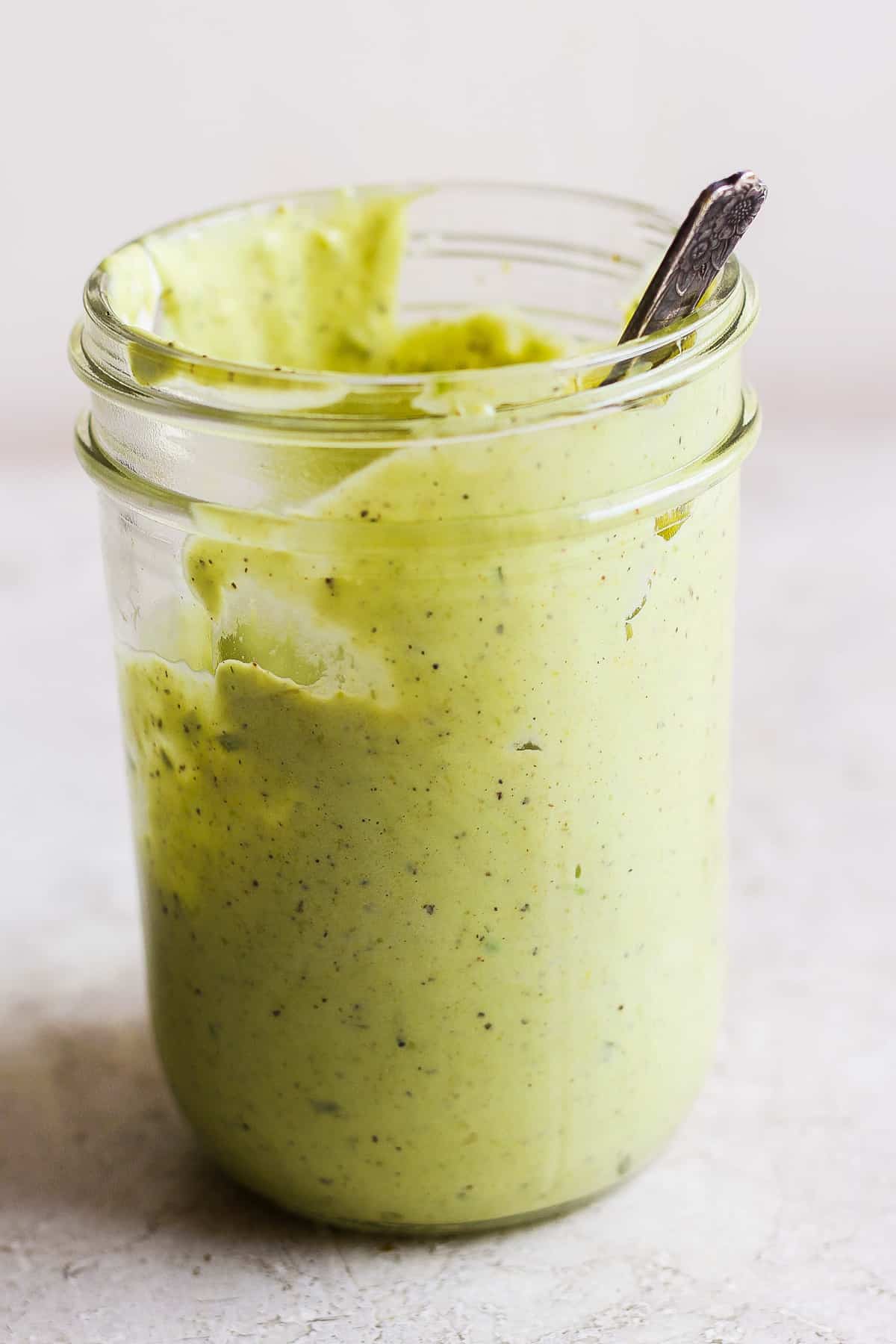 a jar of green sauce with a spoon in it.