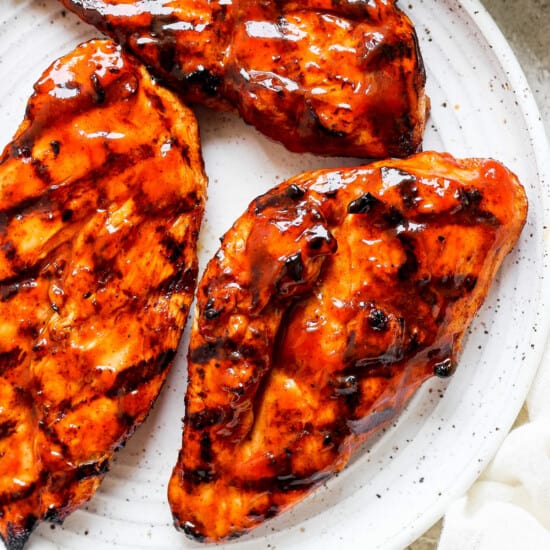 grilled chicken breasts on a white plate with sauce.