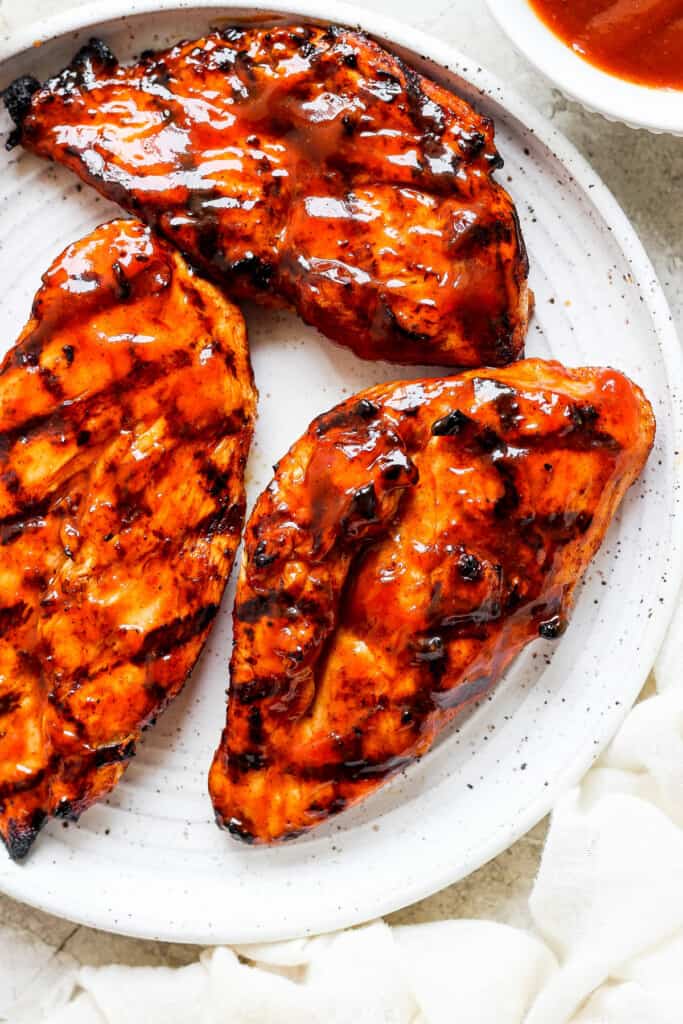 grilled chicken breasts on a white plate with sauce.