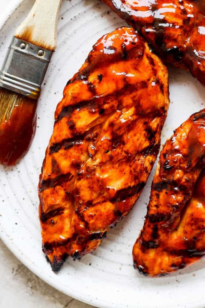 bbq grilled chicken on a white plate with a brush.