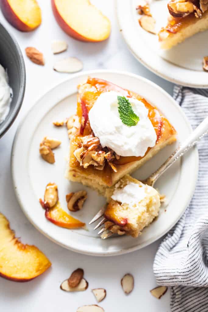 a slice of peach cake with whipped cream and almonds on a plate.